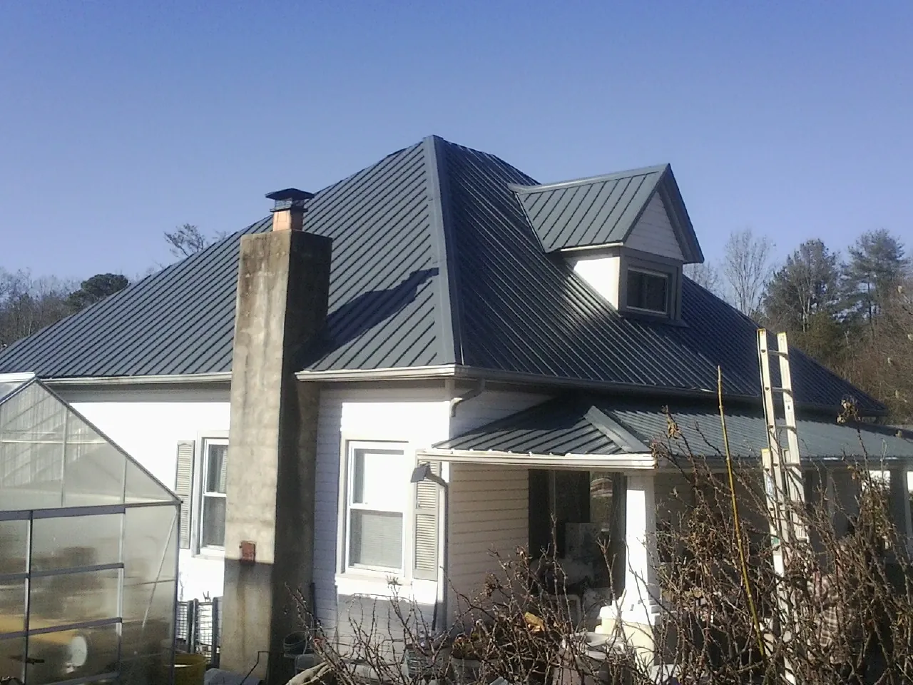 Dark blue standing seam metal roof on a white farmhouse with dormer — Slate & Tile Roof Repair by Roofing Brothers in Round Rock