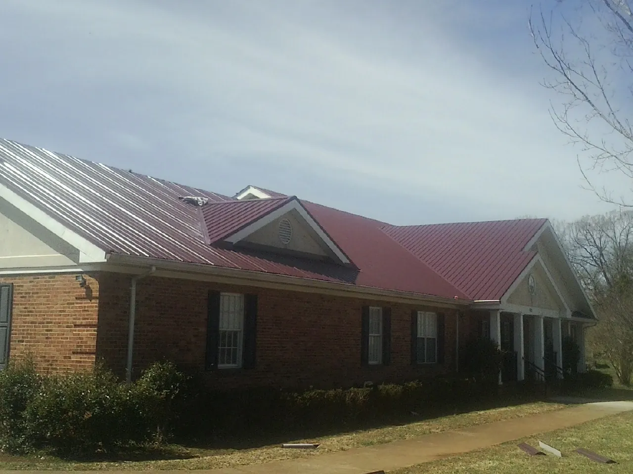 Red metal roof with gabled entries on a long brick building, from a Hail Damage Roof Repair job in Round Rock