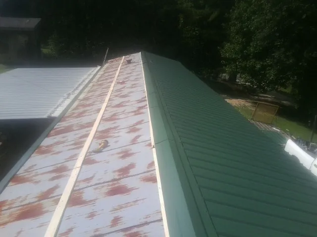 Old rusted panels beside newly installed green metal roofing — Wind Damage Roof Repair by Roofing Brothers in Round Rock