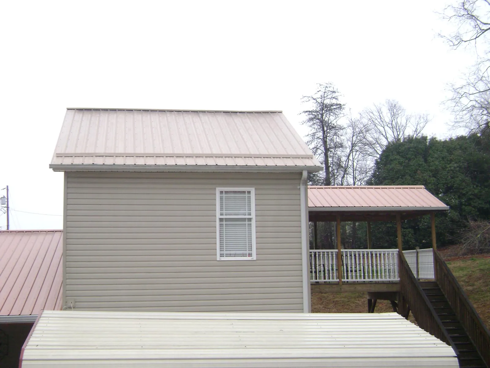 Tan metal roofs on a two story addition and attached porch, from a Roof Replacement job in Round Rock